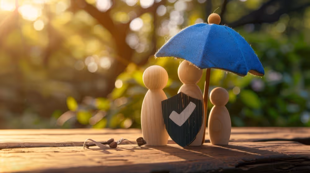 Figurines sous un parapluie derrière un bouclier, illustration de la comparaison des contrats d’assurance vie.