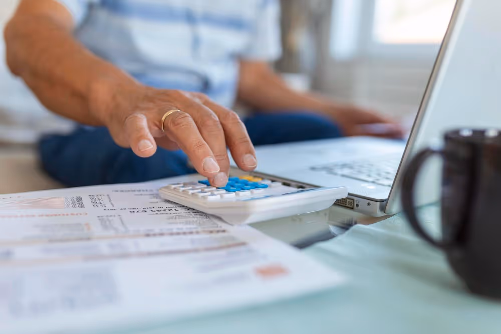 Calculatrice et documents près d’un ordinateur, illustration d’une simulation de remboursement anticipé d’un prêt.