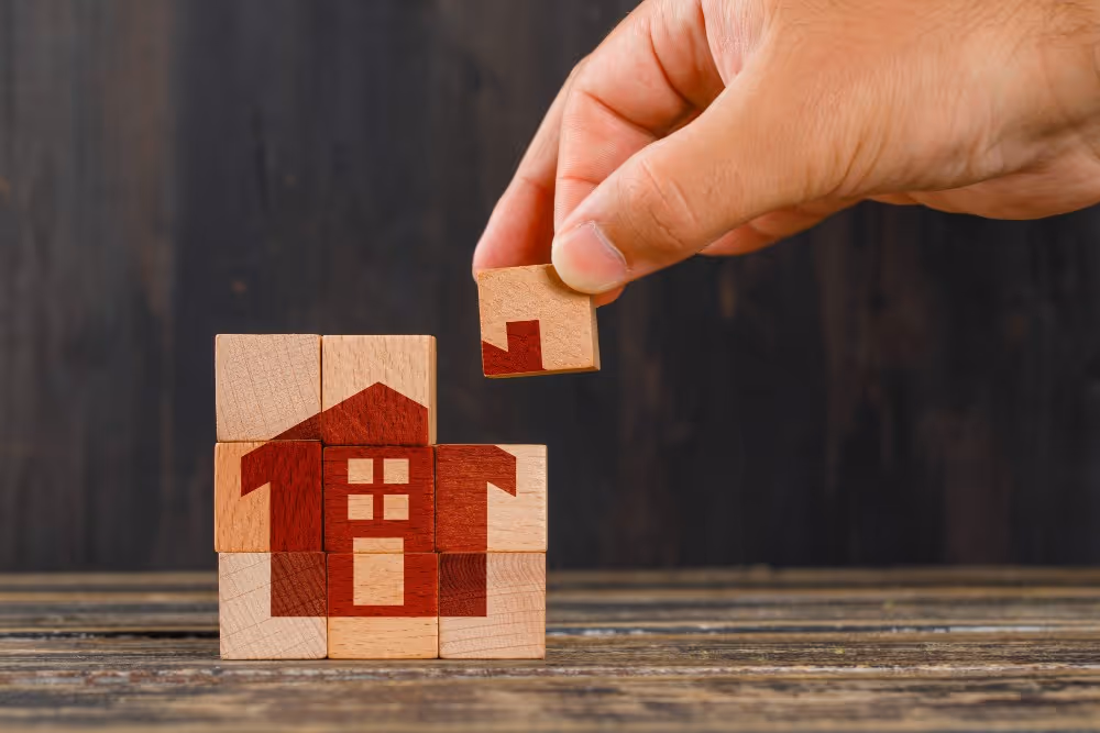 Une maison en cubes de bois dont un élément est retiré, illustration du démembrement entre usufruit et nue-propriété.
