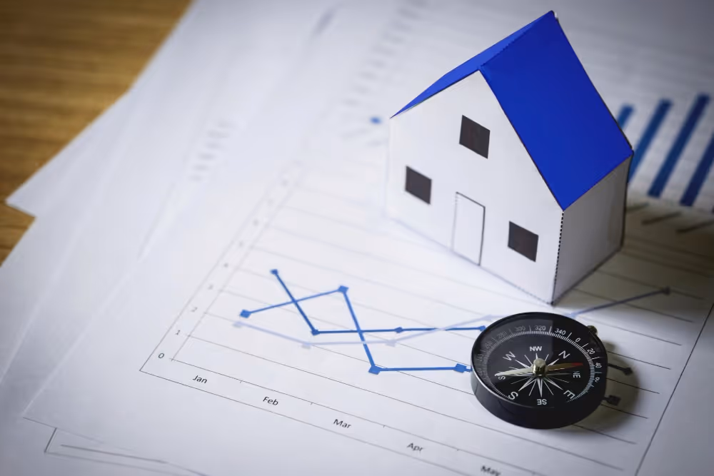 Maquette de maison et boussole sur des graphiques, illustration d’une simulation d’investissement locatif.