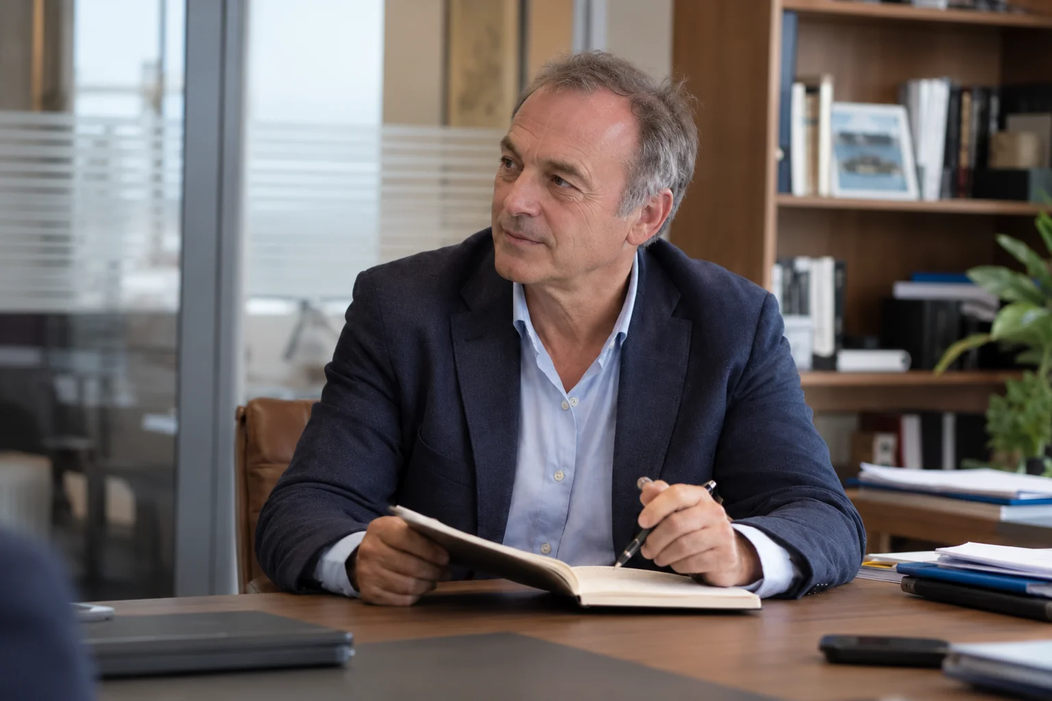 Un entrepreneur d’environ cinquante-cinq ans regarde vers la gauche, un carnet ouvert devant lui.