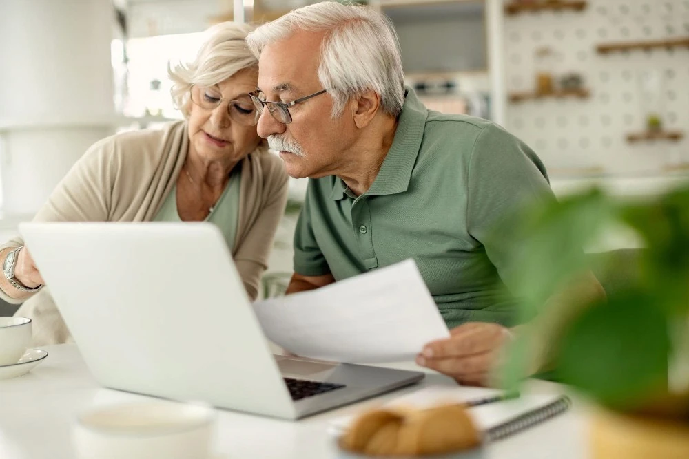 Un couple âgé consulte des documents devant un ordinateur, illustration du suivi de l’augmentation des retraites.