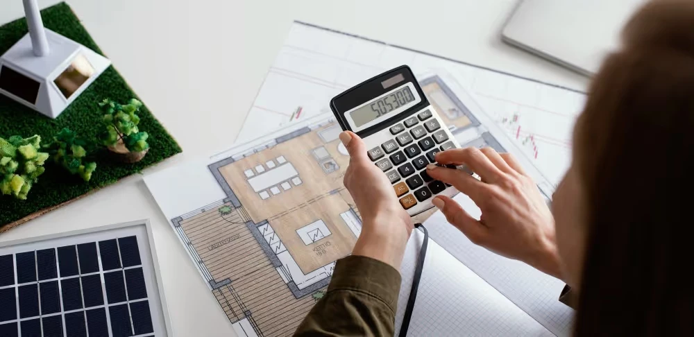 Calculatrice au-dessus d’un plan près d’une maquette de maison, illustration de la simulation du rendement d’une SCPI.