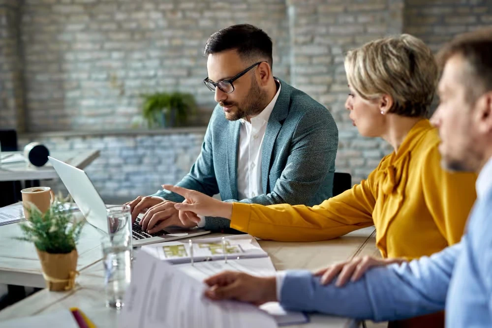 Trois personnes étudient des documents autour d’un bureau, illustration du conseil en investissement financier.