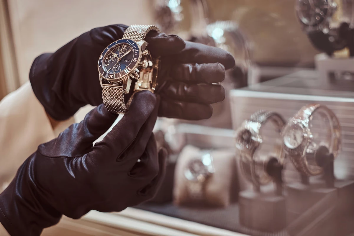 Une montre présentée par des mains gantées devant une vitrine, illustration de l’investissement dans les montres.
