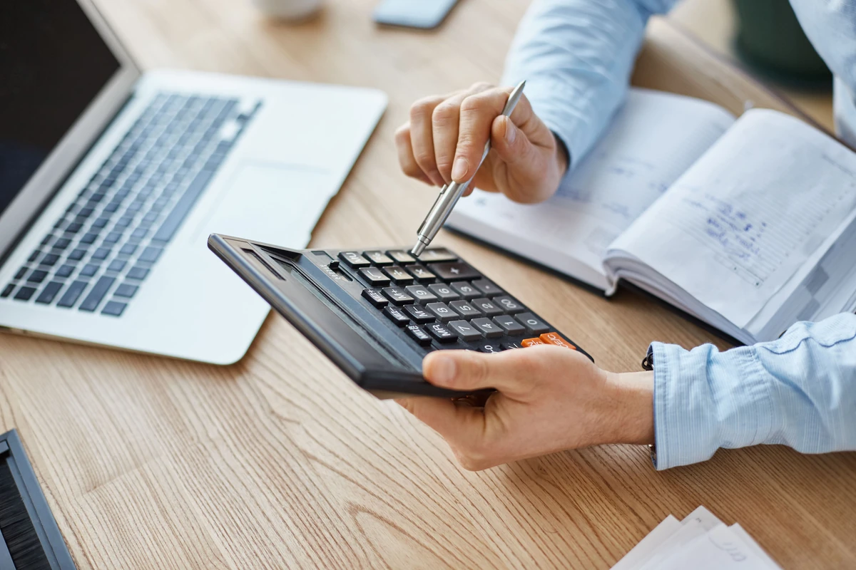 Calculatrice, ordinateur et dossier ouvert illustrant l’évaluation du tarif d’un conseiller en gestion de patrimoine.