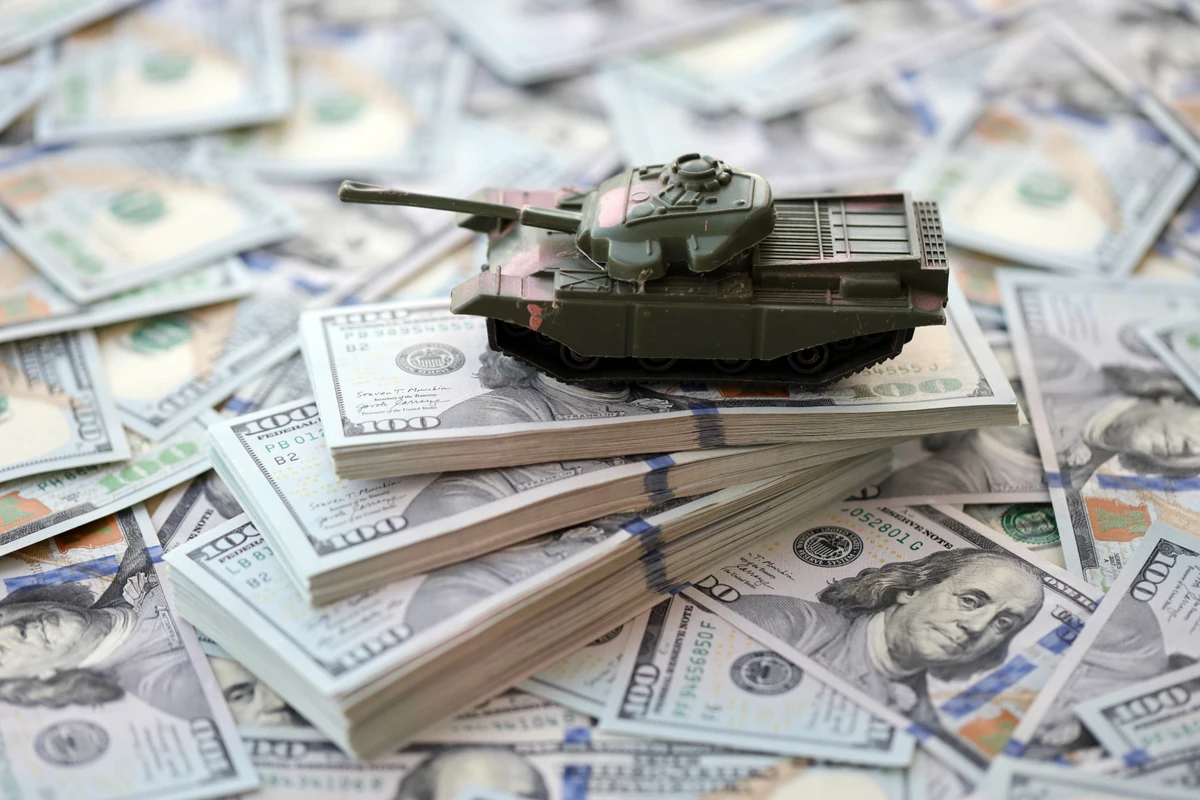 Maquette de char militaire sur des billets de dollars, illustration des risques pour l’épargne en cas de guerre.