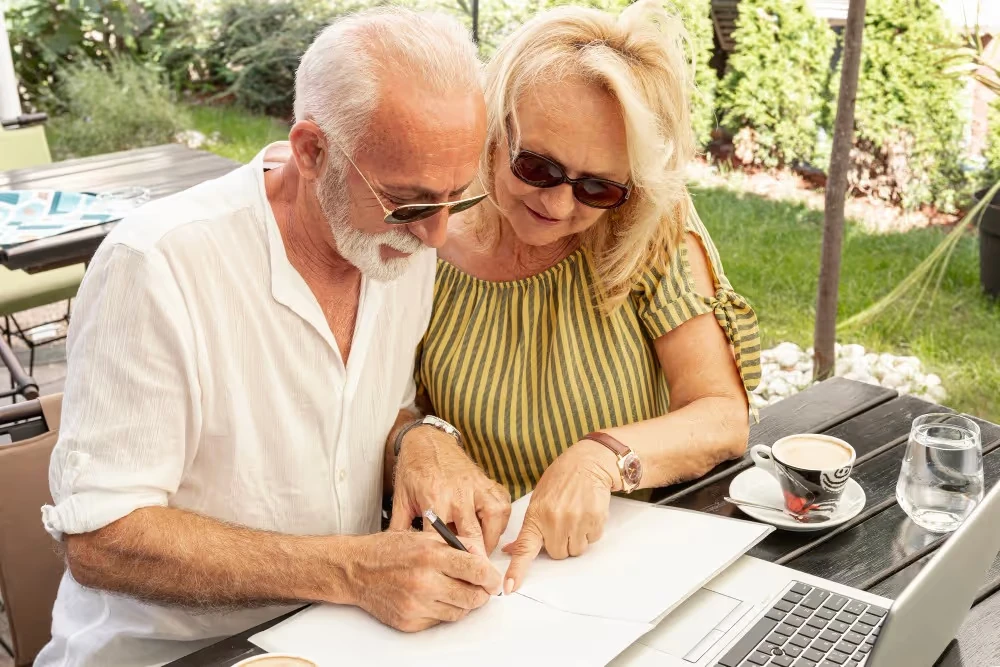 Un couple âgé remplit un document en terrasse, illustration du choix d’un plan d’épargne retraite (PER).
